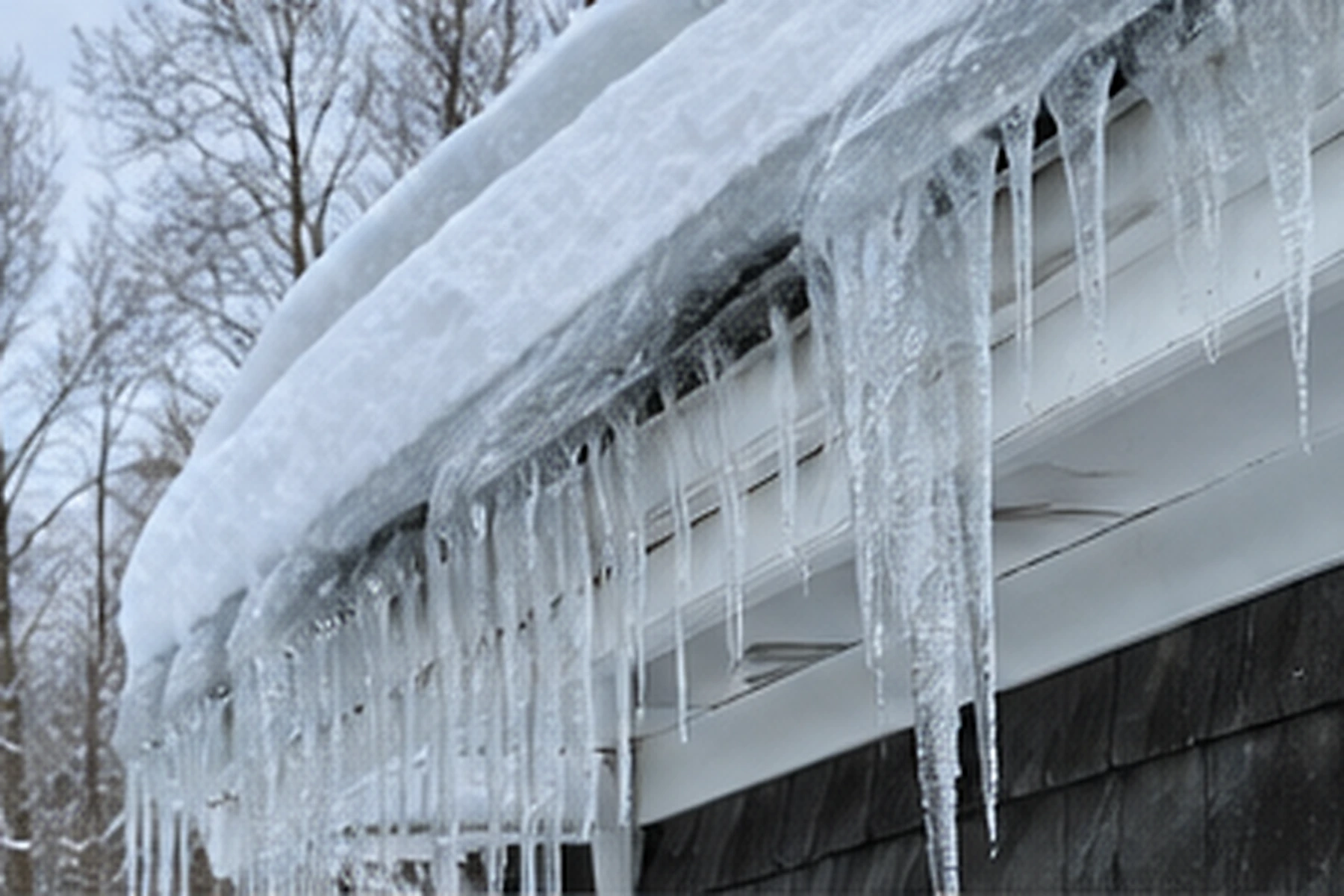 Icicles and a thick ice dam along the eave of a shingled house