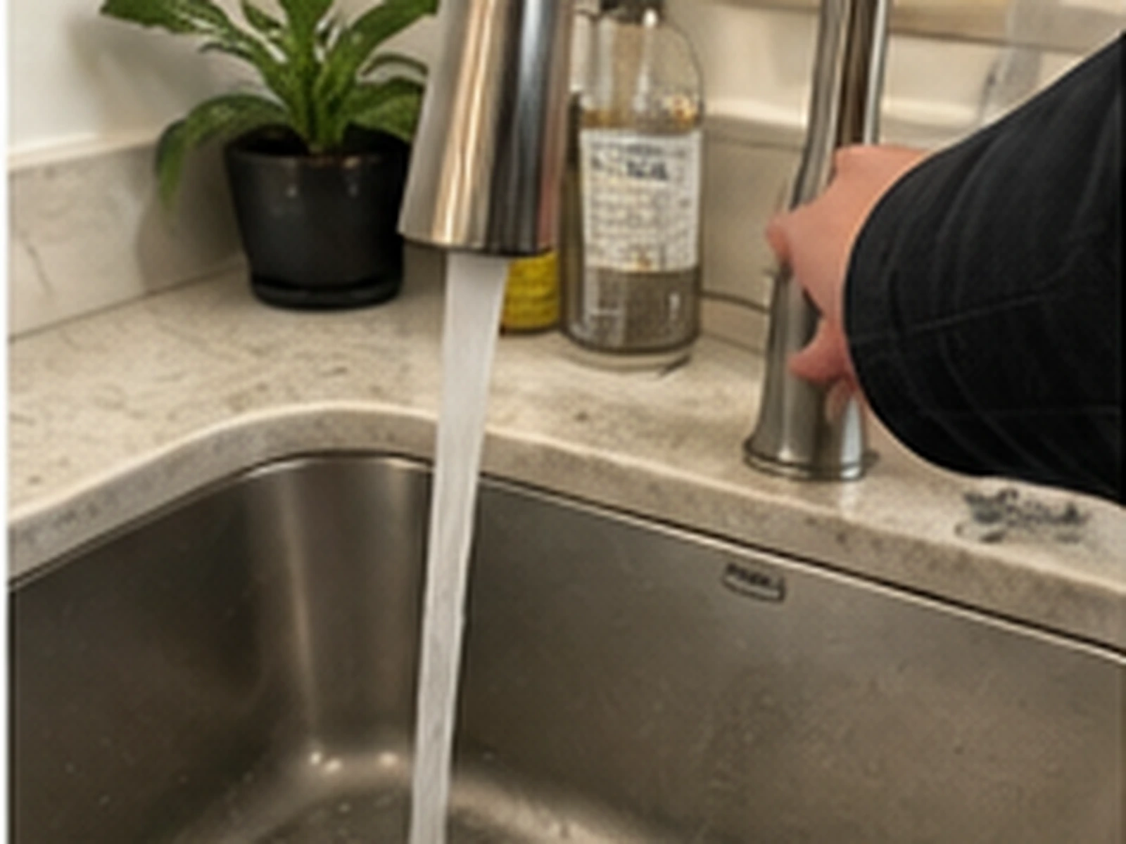 A hand running a kitchen faucet over a steel sink