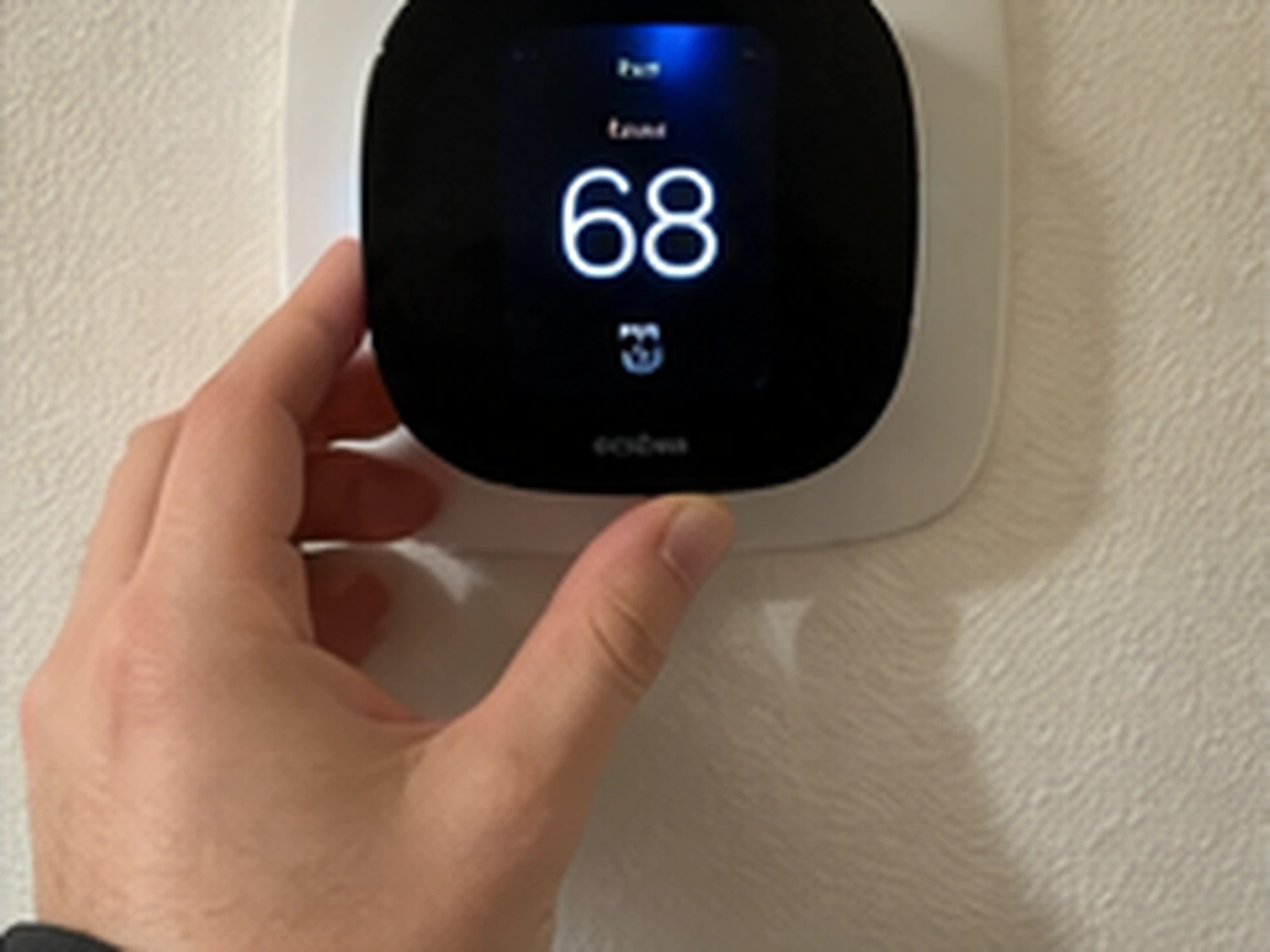 A hand beside a wall thermostat reading 68 degrees